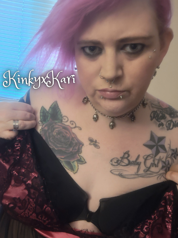 Cam model KinkyxKari KariGrant covering up by holding lingerie over her naked body with a sexy look in her eyes.